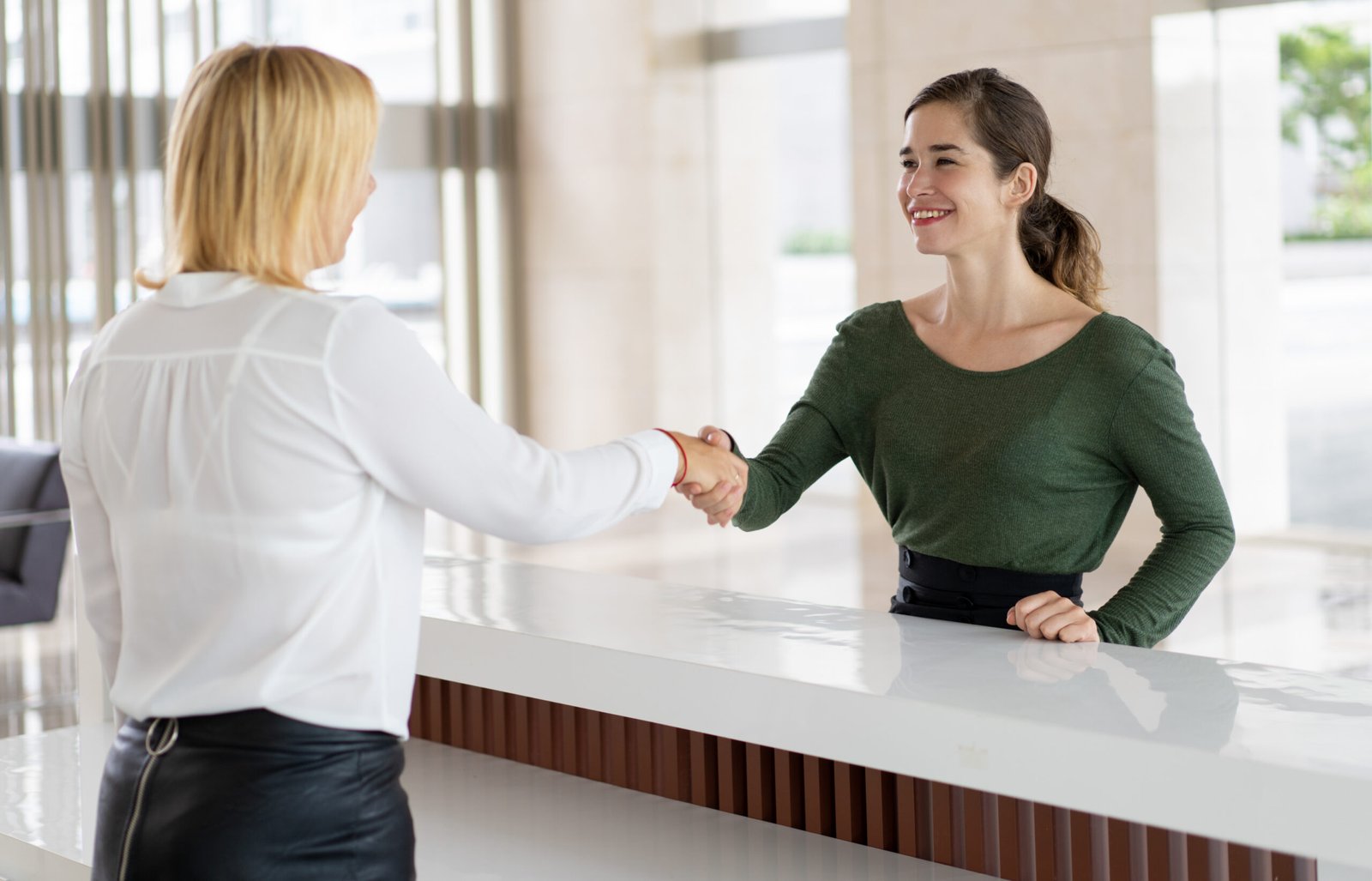 Office receptionist greeting corporate partner Office receptionist greeting corporate partner with handshake. Woman in formal clothing shaking hands over reception counter. Partnership concept