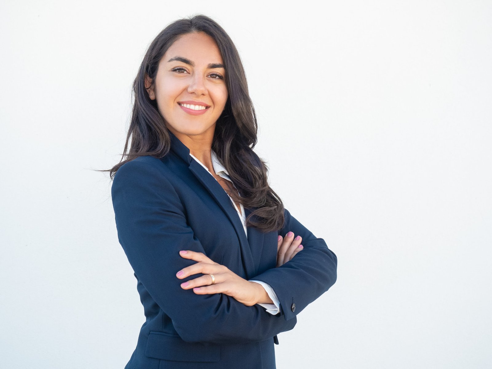 Smiling confident businesswoman posing with arms folded Smiling confident businesswoman posing with arms folded. Happy beautiful black haired young Latin woman in formal suit standing for camera over white studio background. Corporate portrait concept